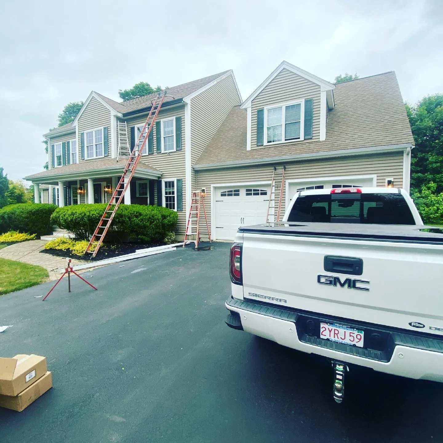 Large colonial home with ladders and truck parked during gutter installation