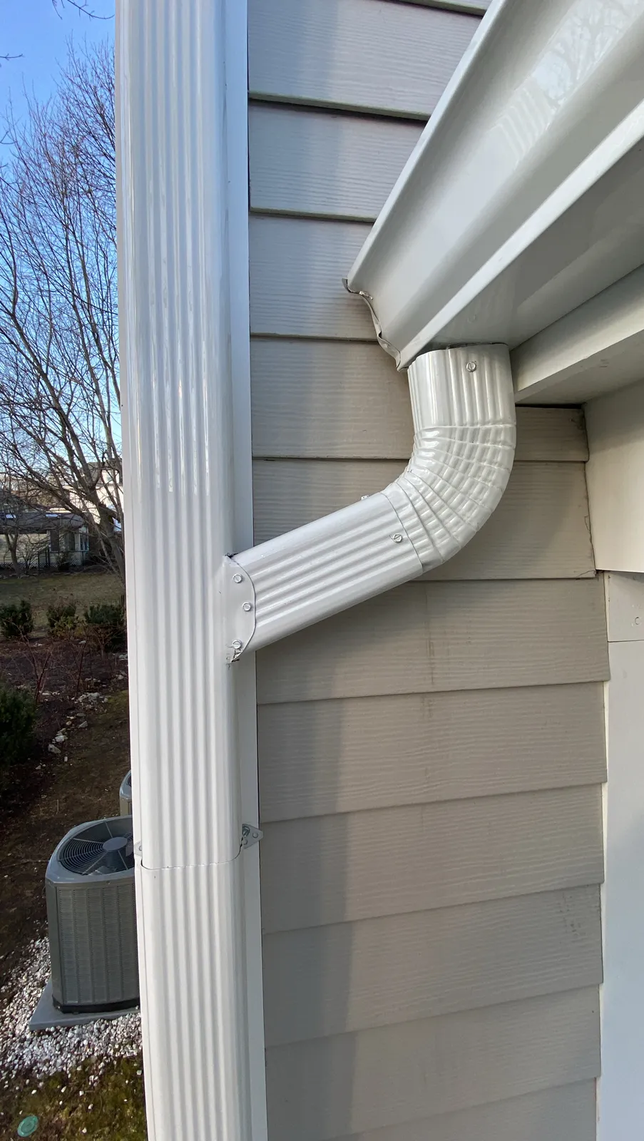 Close-up of a white ribbed downspout elbow connected to a gutter outlet