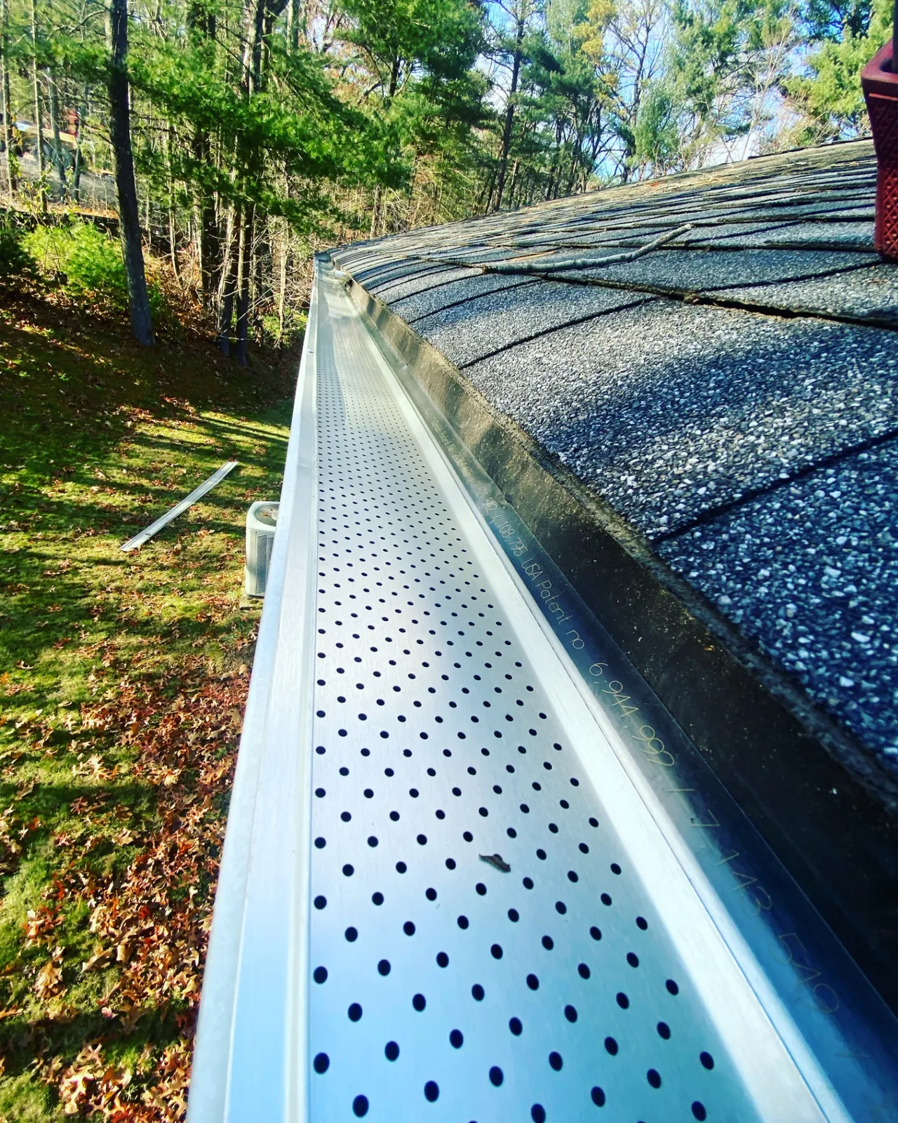 Close-up of a perforated gutter guard installed along an asphalt shingle roof