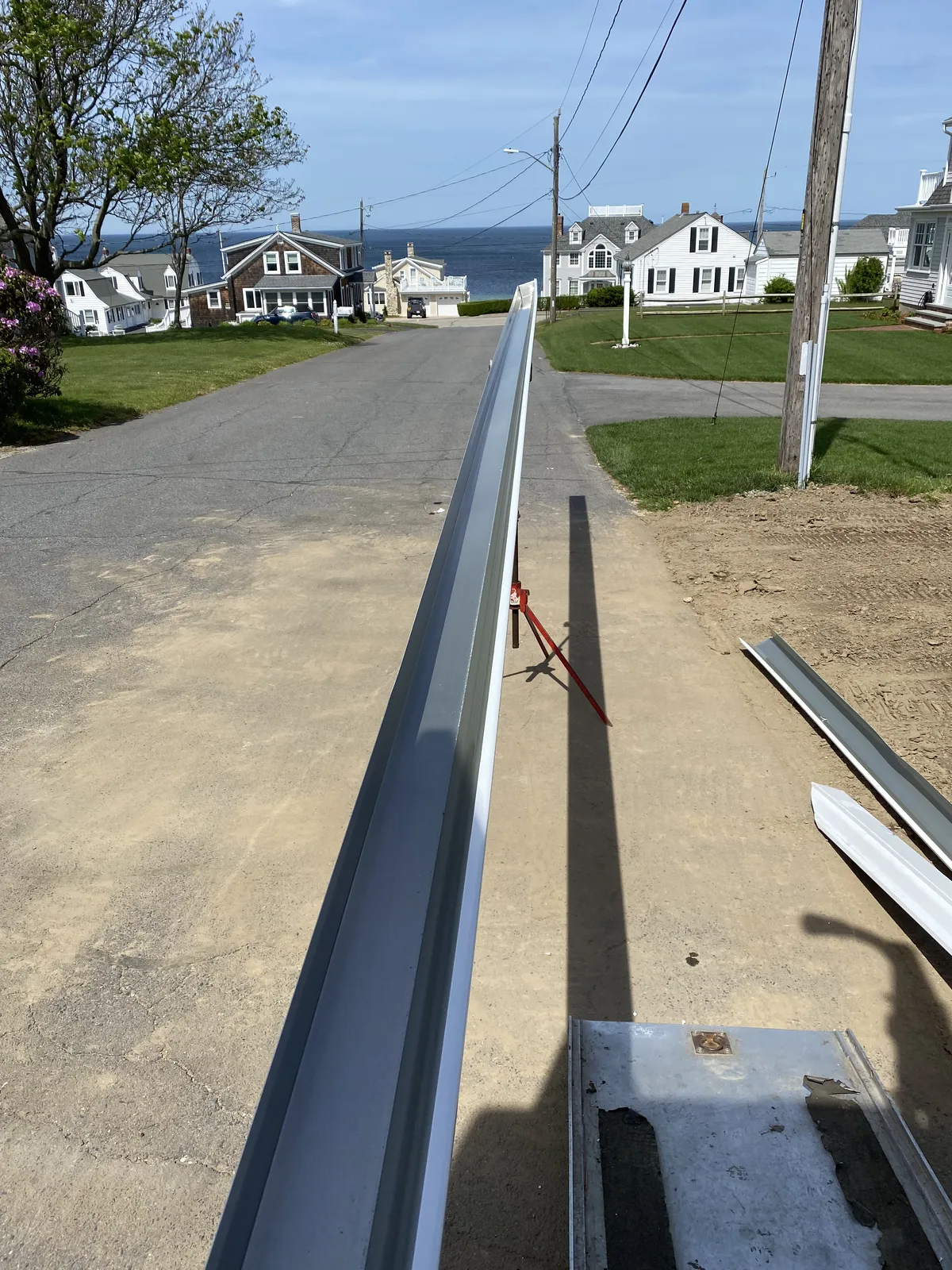 Long freshly fabricated seamless gutter section staged on a coastal street before installation