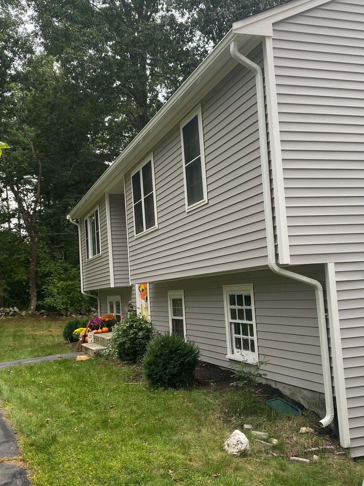 Gray home with newly installed white gutters and downspouts running to grade